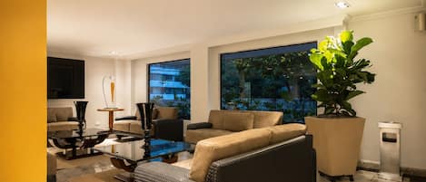 A modern living room with a glass coffee table, beige sofas, and a large potted plant.