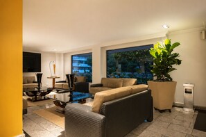 Una sala moderna con una mesa de centro de vidrio, sofás color beige y una planta grande en maceta.