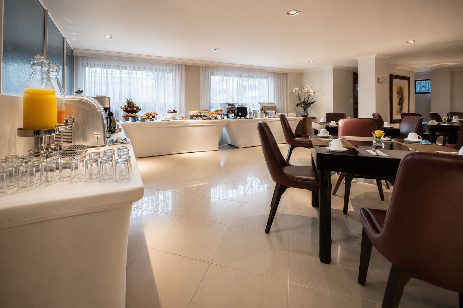 A modern hotel dining area with a buffet setup, a coffee station, and a seating arrangement for guests.