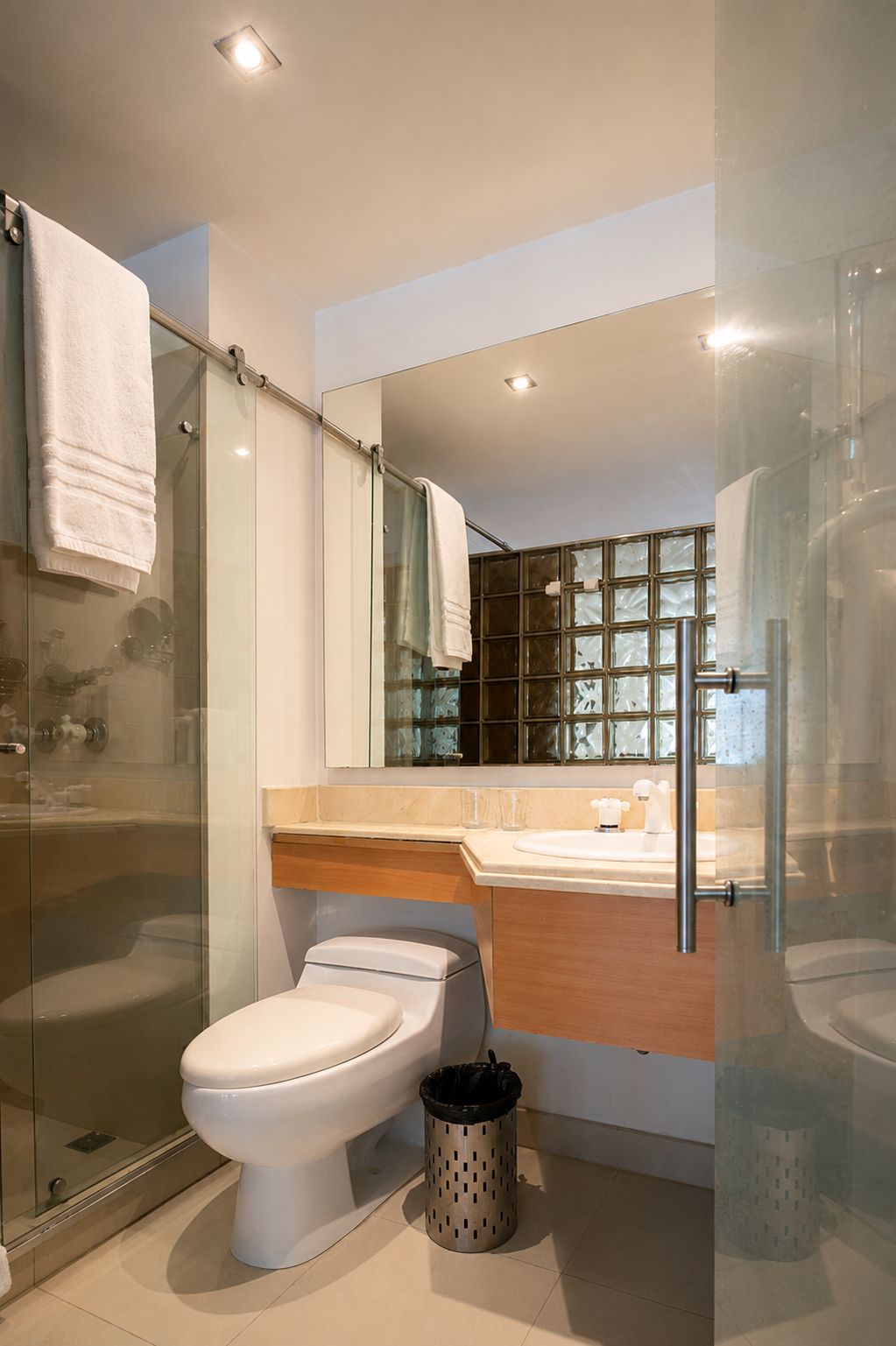 Un baño moderno con ducha envuelta en vidrio, inodoro, lavamanos con espejo y un cubo de basura.
