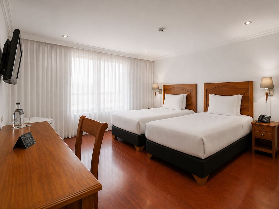 A hotel room with two beds, a wooden desk, a television, and a minibar.