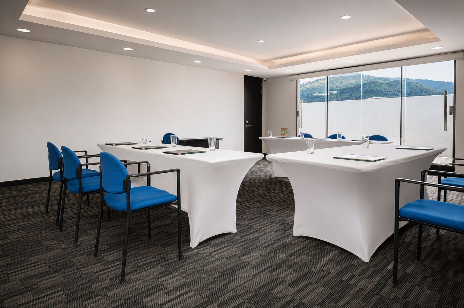 A conference room with two tables, blue chairs, and a view of a lake through large windows.