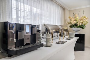 Una estación de café moderna con dos máquinas de espresso, una prensa francesa y un arreglo ornamental de orquídeas.