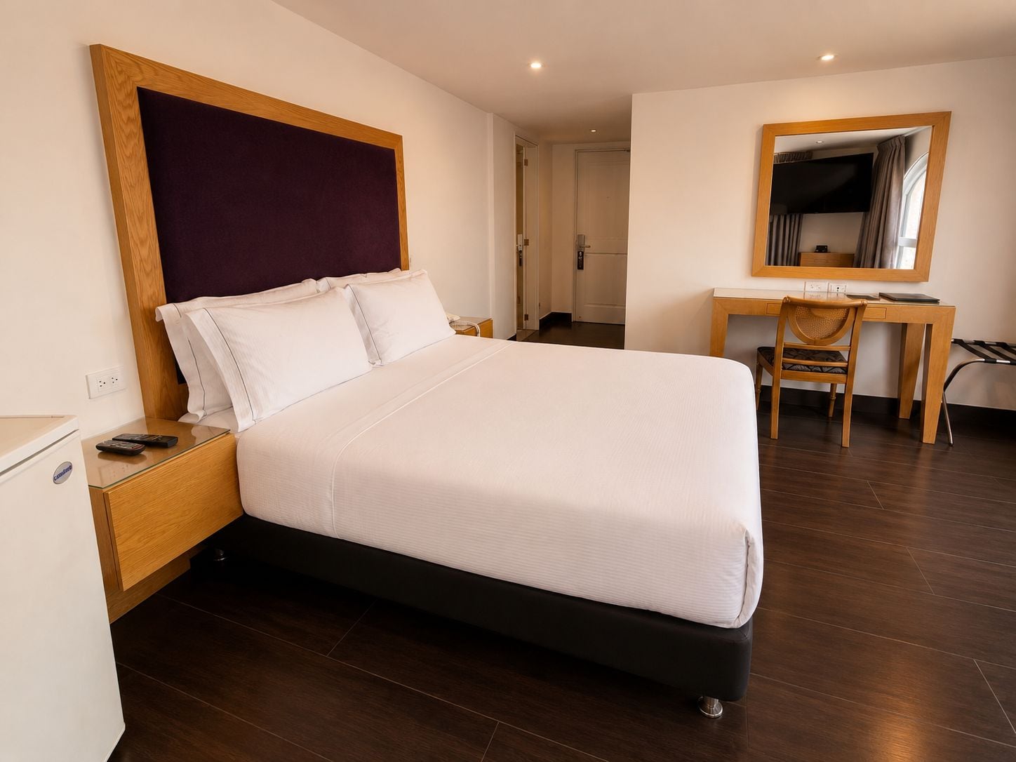 A hotel room with a large bed, a desk, and a mirror.