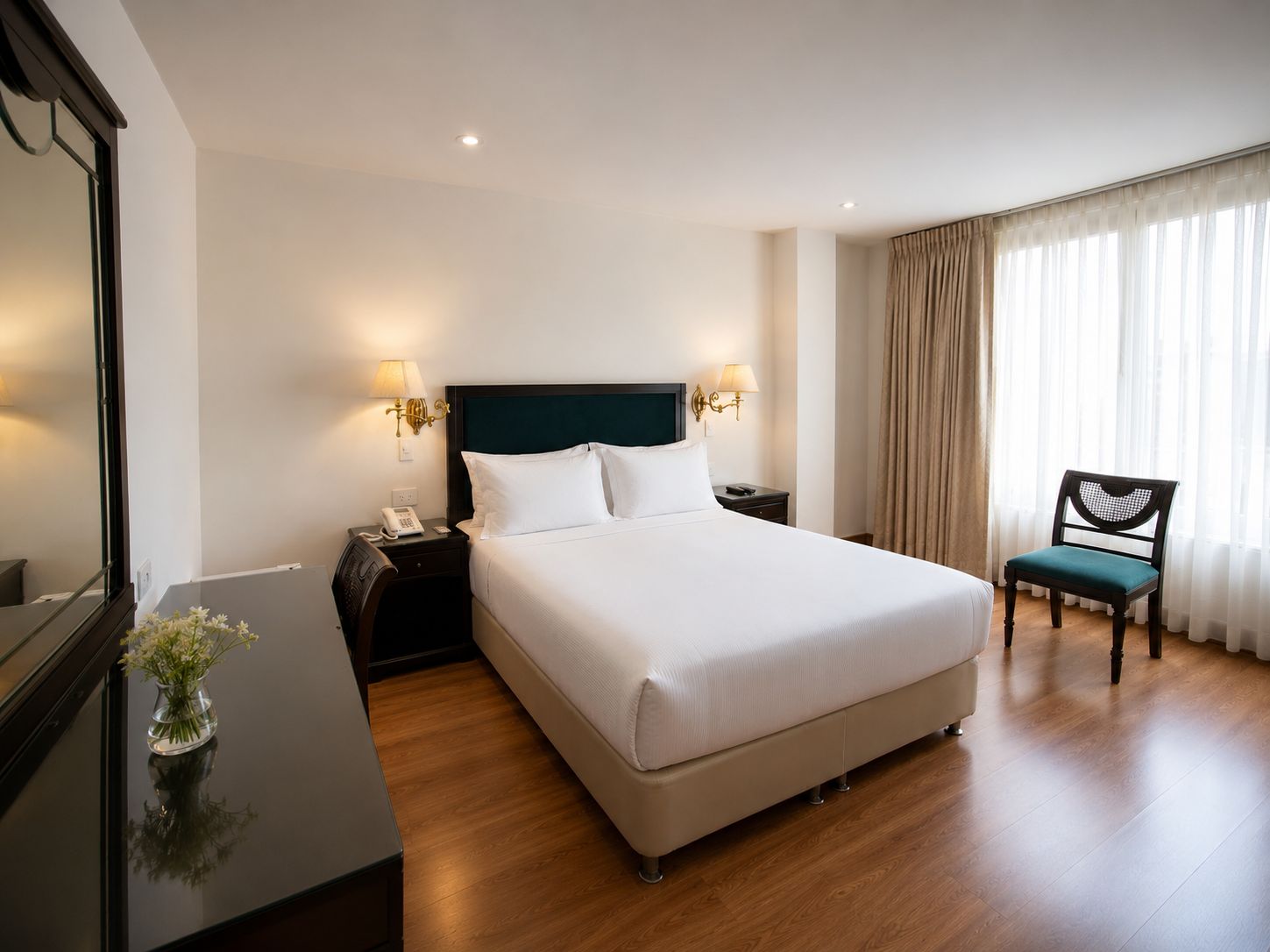Habitación de hotel con una cama grande, mesitas de noche con lámparas, una silla y un espejo.