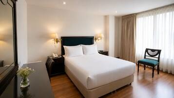 Habitación de hotel con una cama grande, mesitas de noche con lámparas, una silla y un espejo.