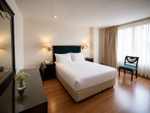 A hotel room with a large bed, bedside tables with lamps, a chair, and a mirror.