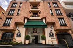 Fachada de hotel con un toldo verde, varios balcones con barandas de hierro forjado y un cartel que indica 'Hotel Le Manoir'.