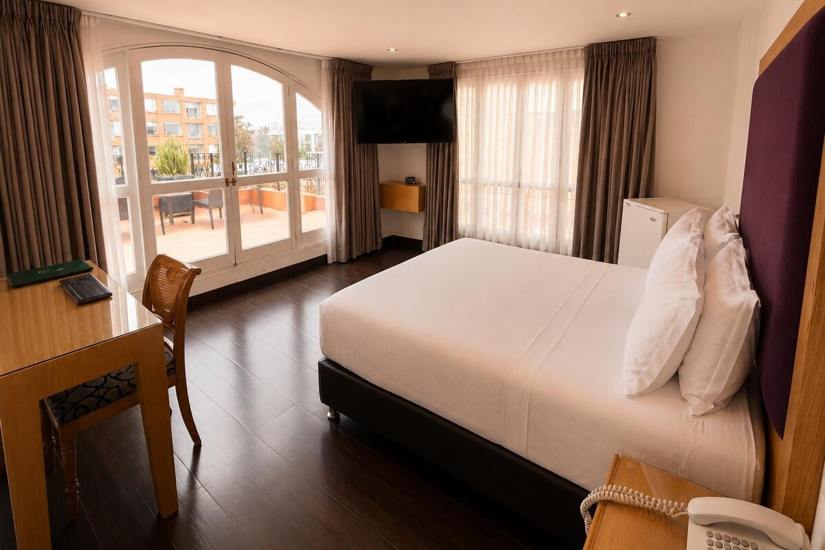 Una habitación de hotel con una cama grande, un escritorio con una silla, un teléfono y un televisor.