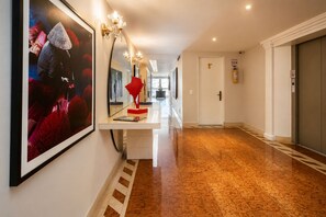 Un pasillo de hotel con piso pulido, un mostrador de recepción, obras de arte en la pared y una puerta con extintor.