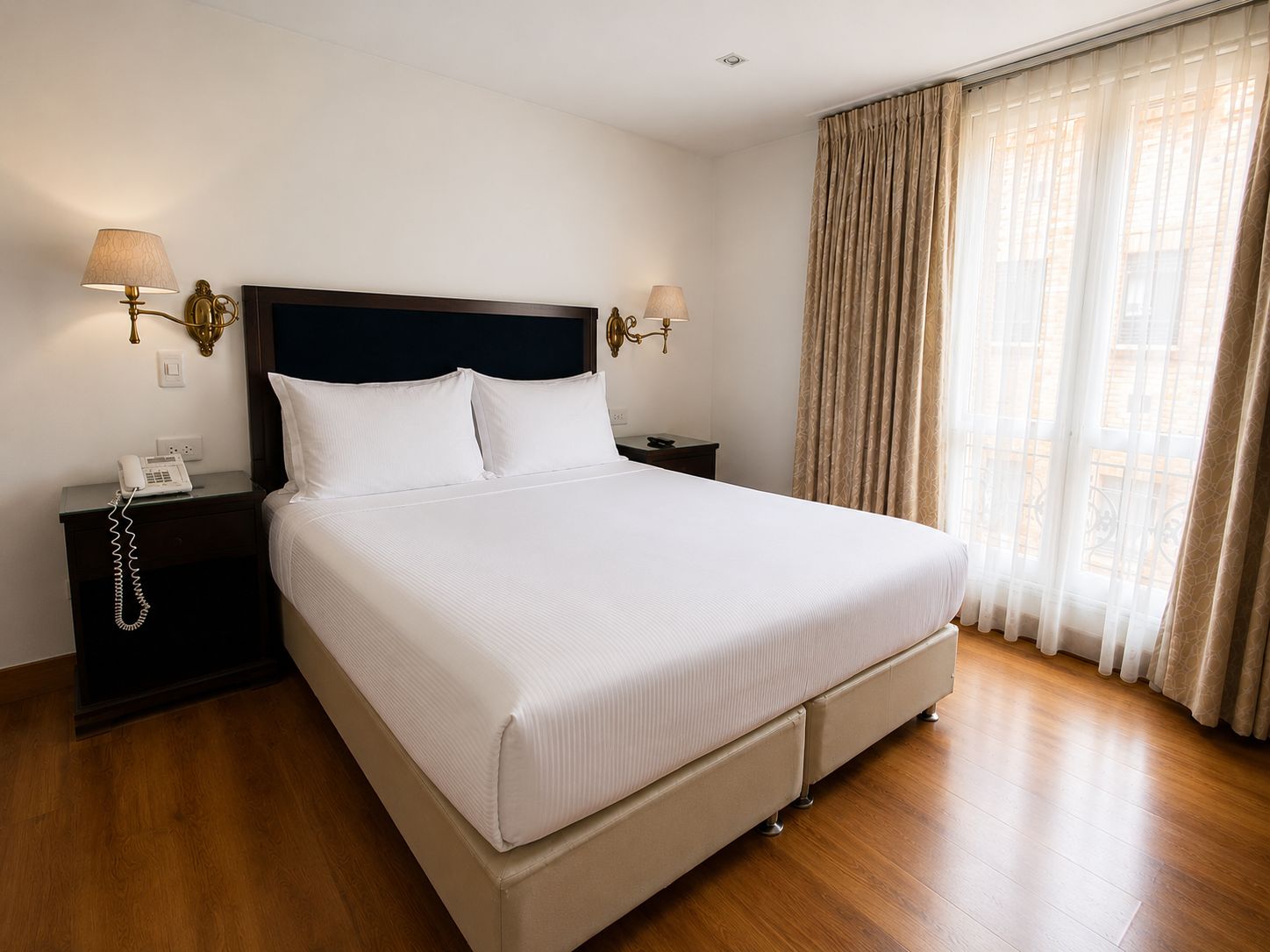 A hotel room with a large bed, two bedside tables, a telephone, and a window with curtains.