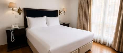 A hotel room with a large bed, two bedside tables, a telephone, and a window with curtains.