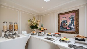 Montaje de bufé con distintas estaciones de comida, que incluyen frutas, pasteles y un cuadro en la pared.