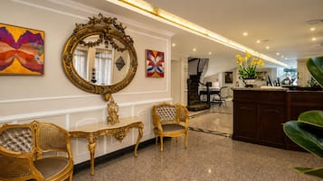 Un vestíbulo de hotel con muebles dorados ornamentados, un espejo grande y obras de arte moderno.