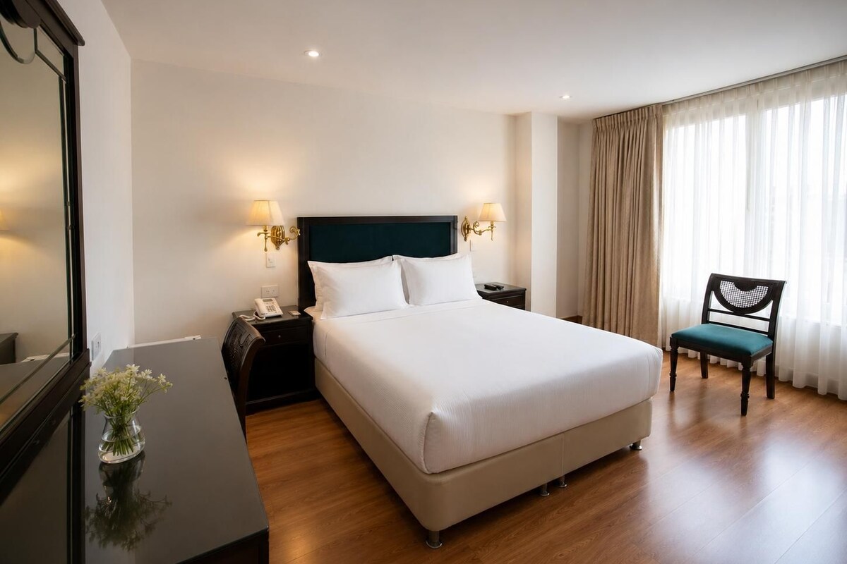 Habitación de hotel con cama, lámparas de noche, una silla y un escritorio con un florero.
