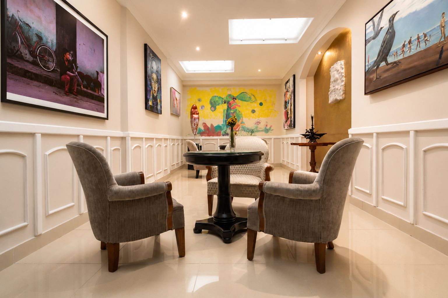 Un pasillo de hotel con un área de comedor que incluye una mesa redonda y cuatro sillas, obras de arte en las paredes y un tragaluz en el techo.