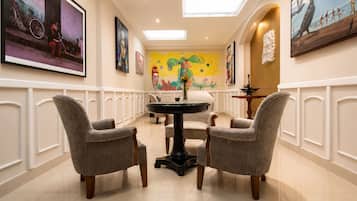 Un couloir d’hôtel avec un espace repas comprenant une table ronde et quatre chaises, des œuvres d’art aux murs et une lucarne au plafond.