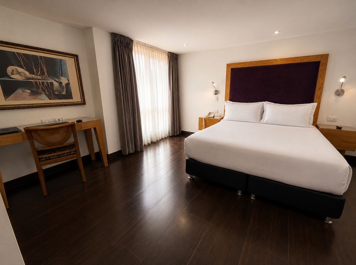 A hotel room with a large bed, a desk, a chair, a painting on the wall, and a window with curtains.