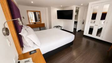 A hotel room with a bed, a bedside telephone, a mirror, a TV mounted on the wall, and a wardrobe with glass doors.
