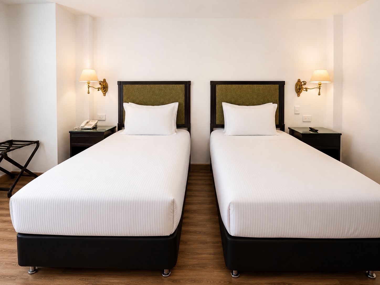 A hotel room with two single beds, bedside tables with lamps, a desk, and a chair.
