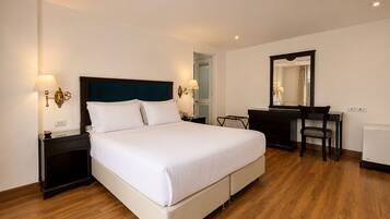 Una habitación de hotel con cama, mesitas de noche, escritorio, silla, espejo y radiador.