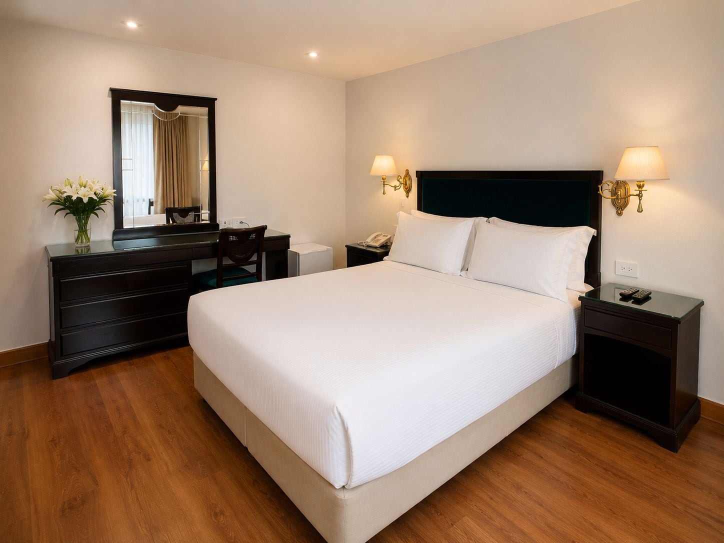 Une chambre d’hôtel avec un grand lit, une commode, un bureau, une chaise, un miroir et des lampes de chevet.