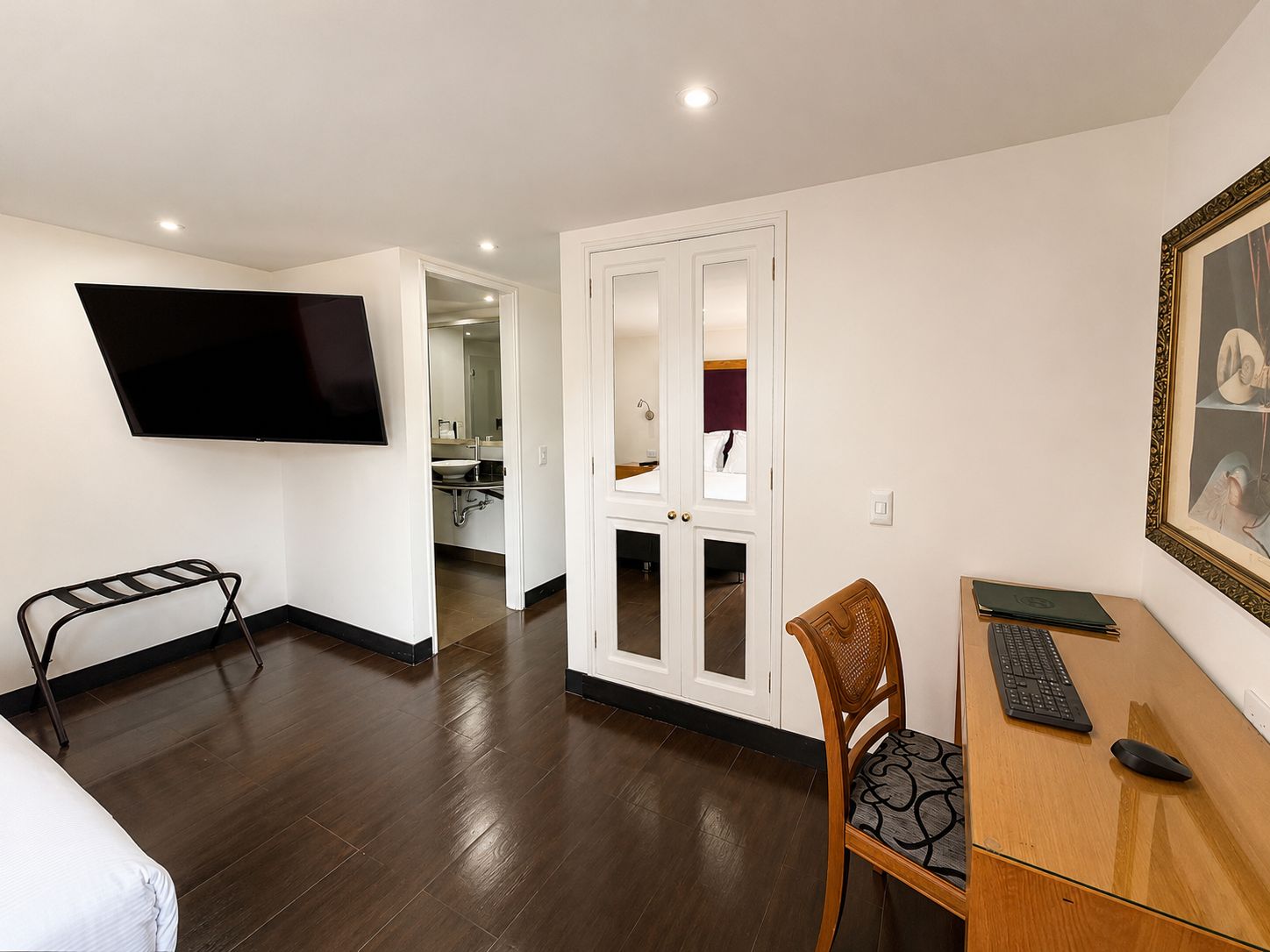 Habitación de hotel con cama, escritorio con computadora, silla, televisor montado en la pared y puerta que da a un baño.