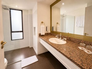 Une salle de bain moderne avec un grand miroir, un comptoir en granit, un lavabo et une douche.