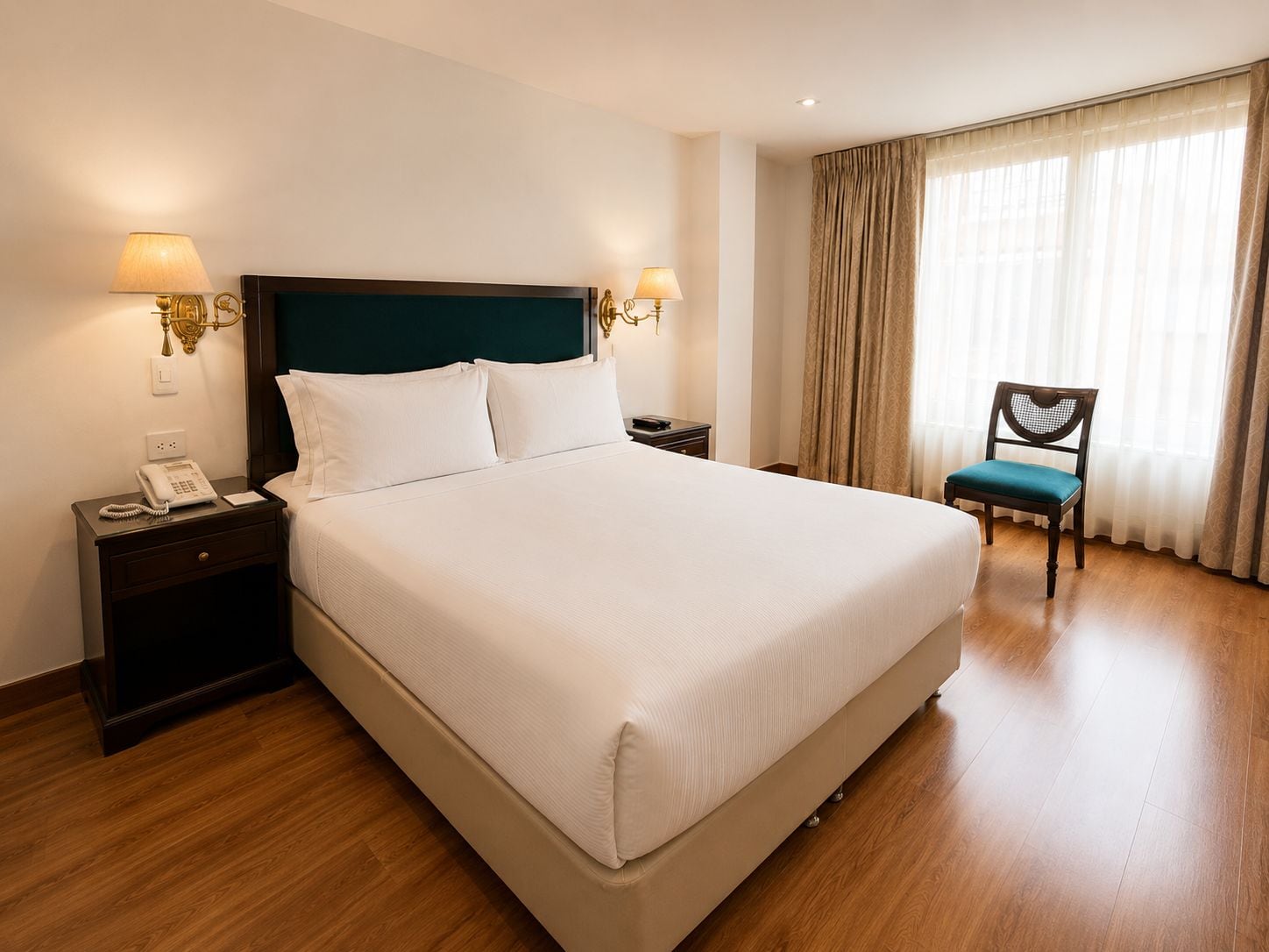 A hotel room with a large bed, bedside lamps, a telephone, a chair, and a window with curtains.
