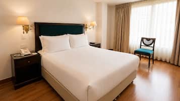 Habitació d'hotel amb un llit gran, abacines, un telèfon, una cadira i una finestra amb cortines.