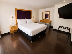 Habitación de hotel con una cama grande, mesitas de noche, un escritorio, una silla, un televisor y un estante pequeño.