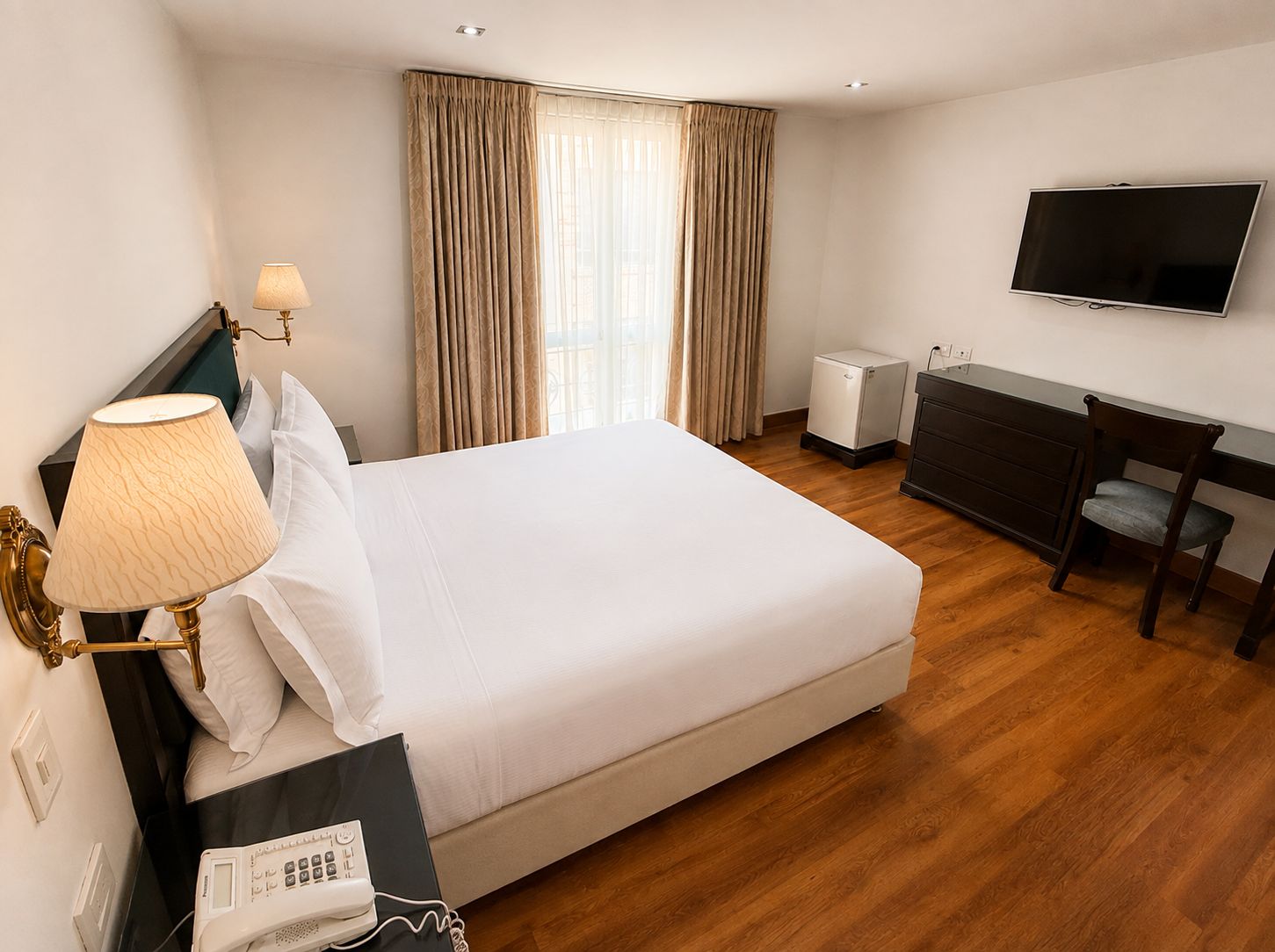 Ein Hotelzimmer mit Bett, Nachttischlampe, Schreibtisch, Stuhl, Fernseher und einem kleinen Heizgerät.