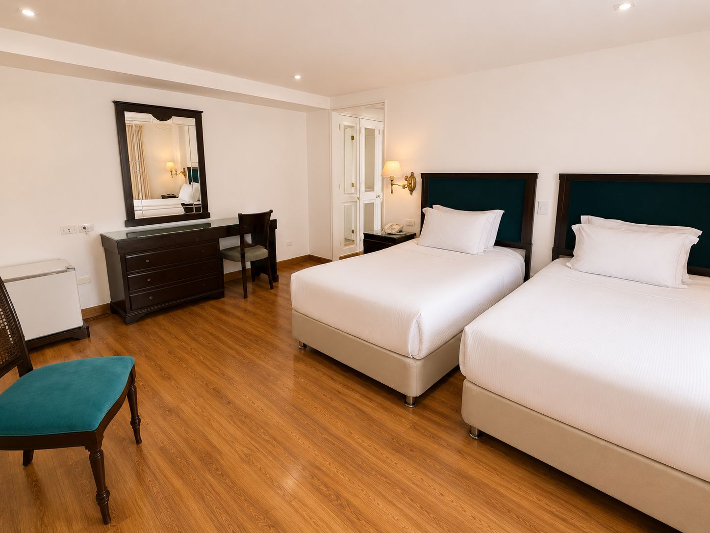 A hotel room with two beds, a dresser, a desk, and a chair.