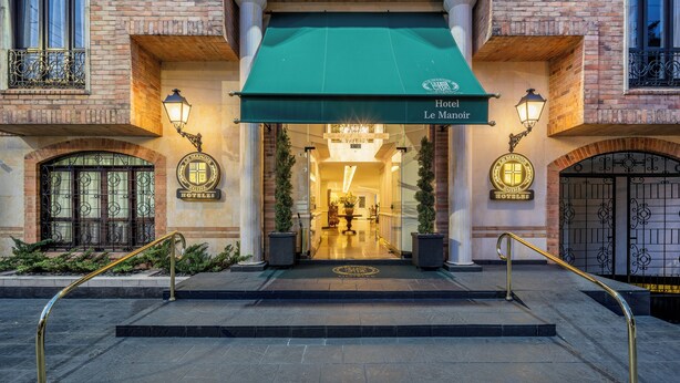 La entrada del Hotel Le Manoir, con un toldo verde, una gran escalera y una reja de hierro forjado.