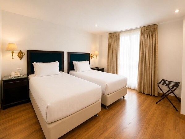 A hotel room with two beds, bedside lamps, a telephone, a window with curtains, and a wooden floor.