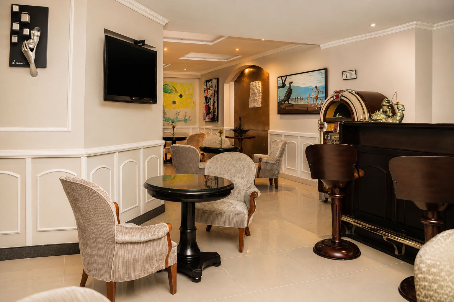 A hotel lobby with a round table, several upholstered chairs, a flat-screen TV mounted on the wall, and a piano.