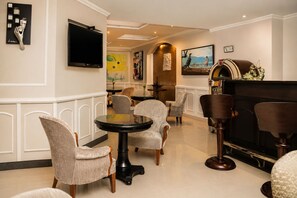 A hotel lobby with a round table, several upholstered chairs, a flat-screen TV mounted on the wall, and a piano. - Hotel Le Manoir Bogota (Bogotá)