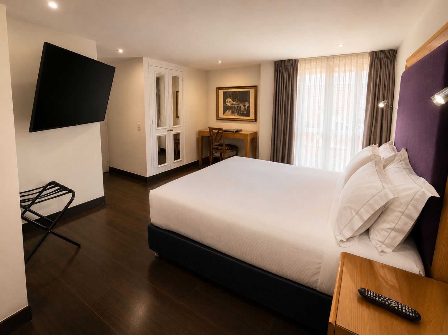 Une chambre d’hôtel avec un lit, un bureau, une chaise, une télévision et une fenêtre avec des rideaux.