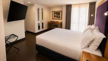 A hotel room with a bed, a desk, a chair, a television, and a window with curtains.
