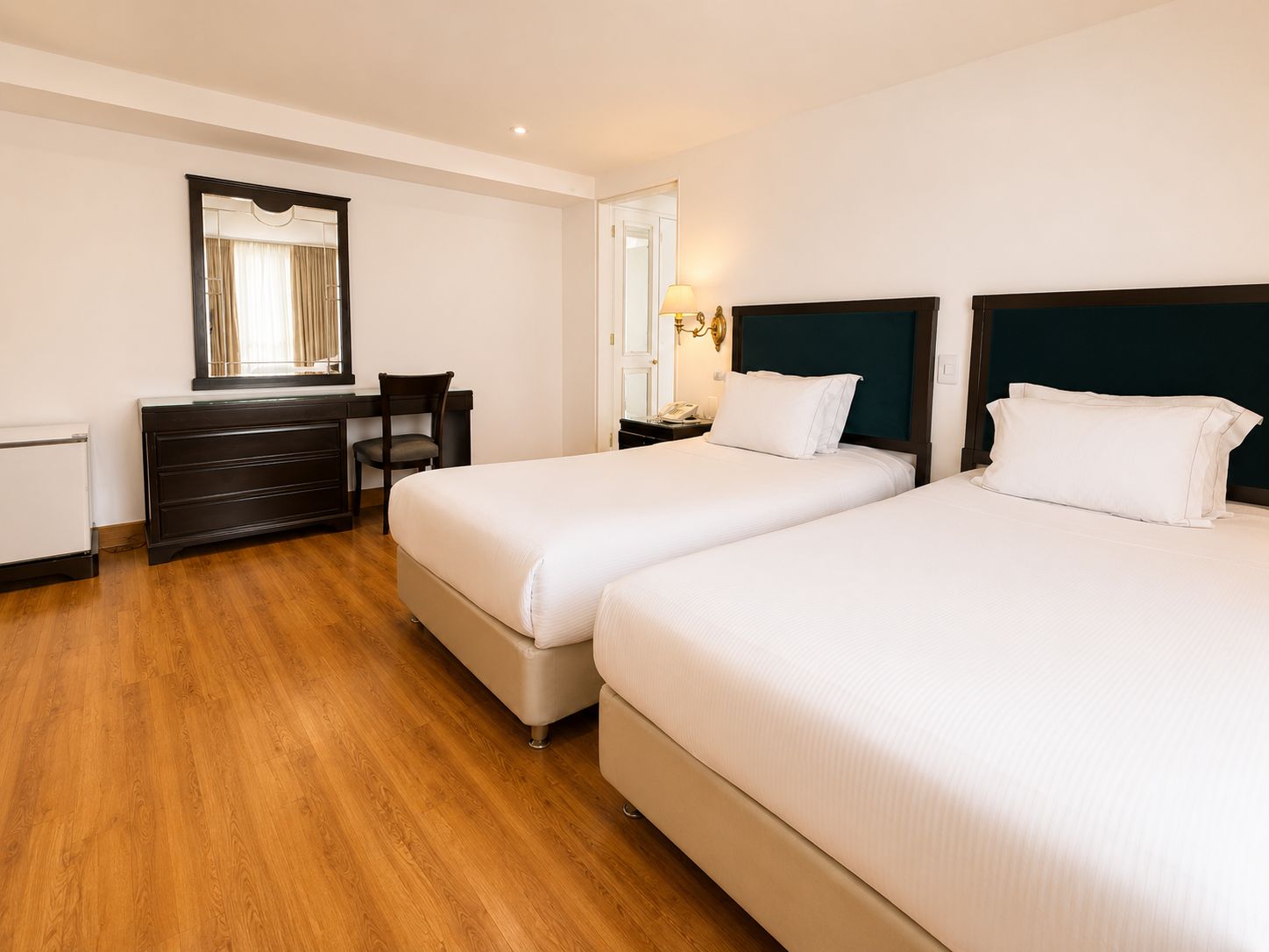 A hotel room with two beds, a desk, a chair, a dresser, and a mirror.