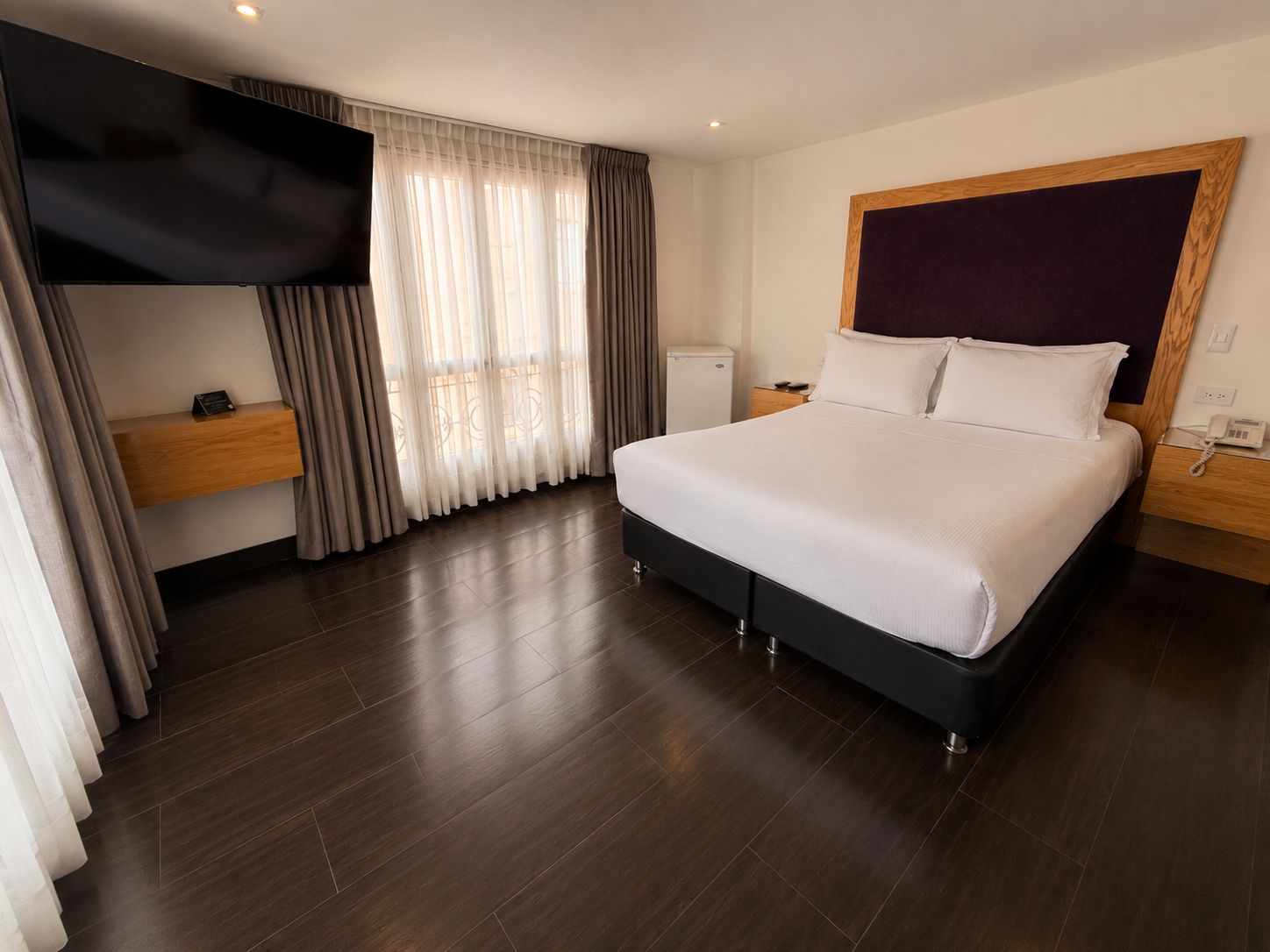 Habitación de hotel moderna con una cama grande, un televisor de pantalla plana, una mesita de noche y un escritorio pequeño con teléfono.