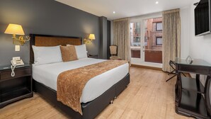 Habitación de hotel con una cama grande, lámparas de noche, un escritorio y vistas a la ciudad desde la ventana.