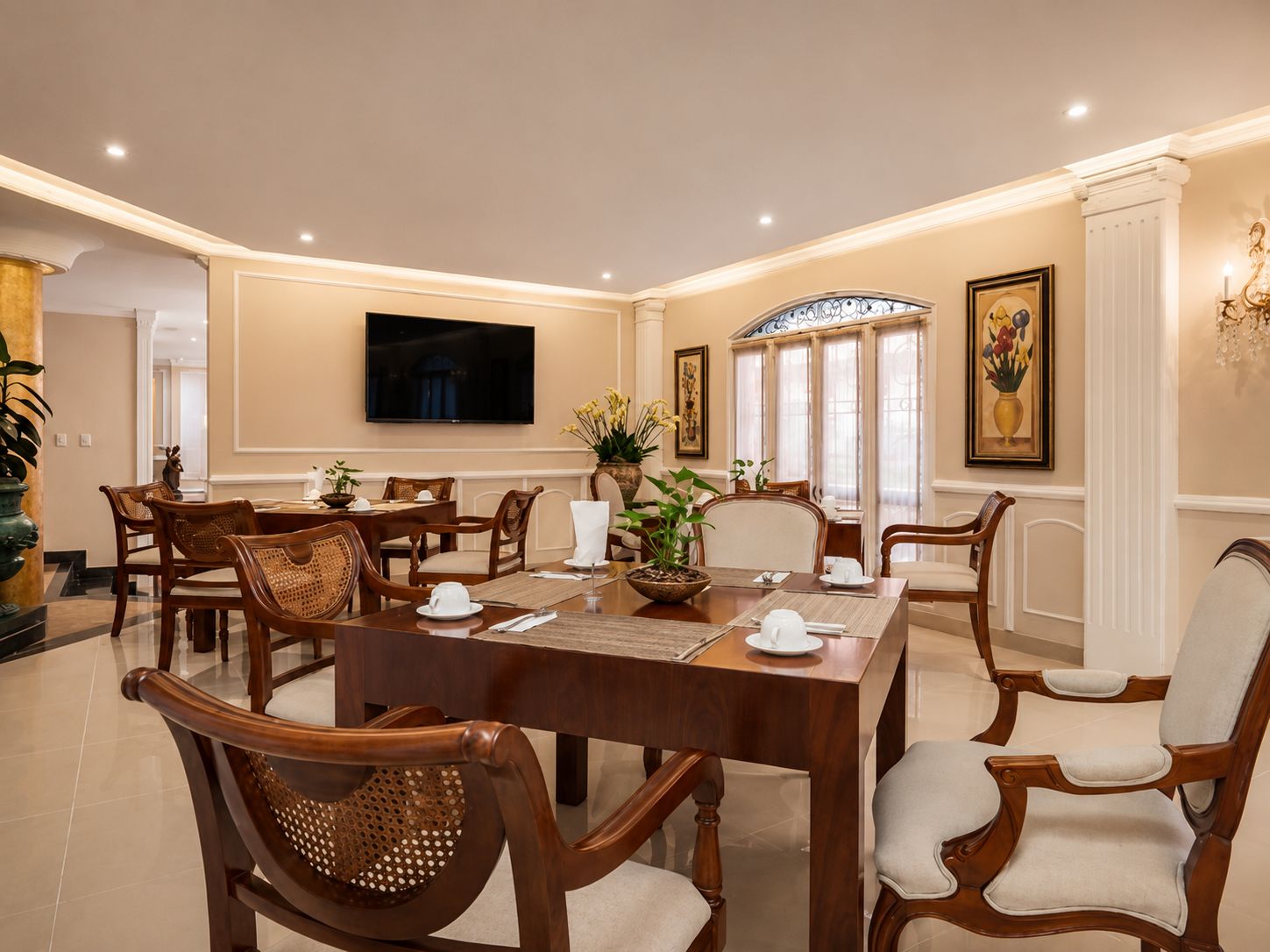 A formal dining room with a large table, multiple chairs, and a television mounted on the wall.
