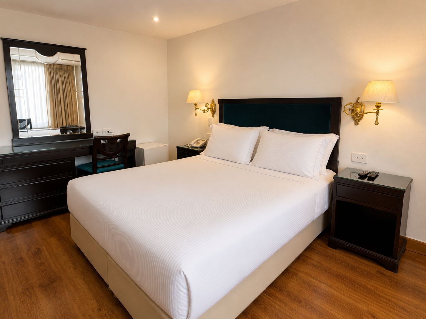 Ein Hotelzimmer mit einem großen Bett, einem Schminktisch, einem Spiegel, zwei Nachttischlampen und einem Telefon.