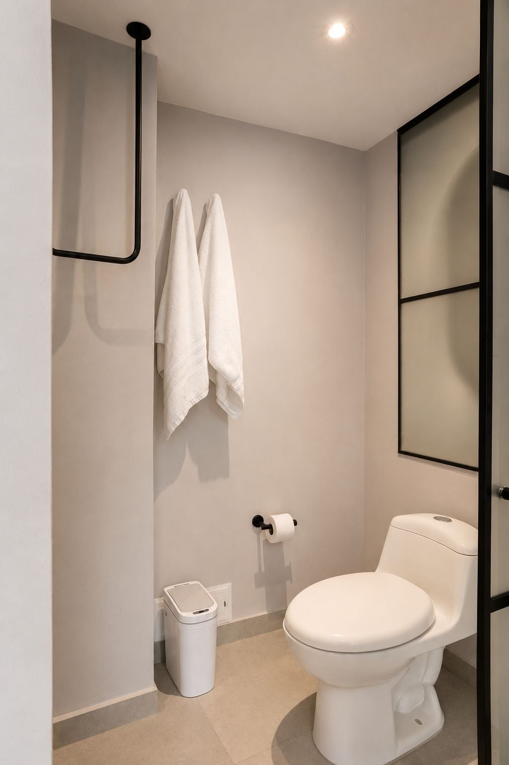 A modern bathroom with a toilet, a trash bin, and a towel rack.