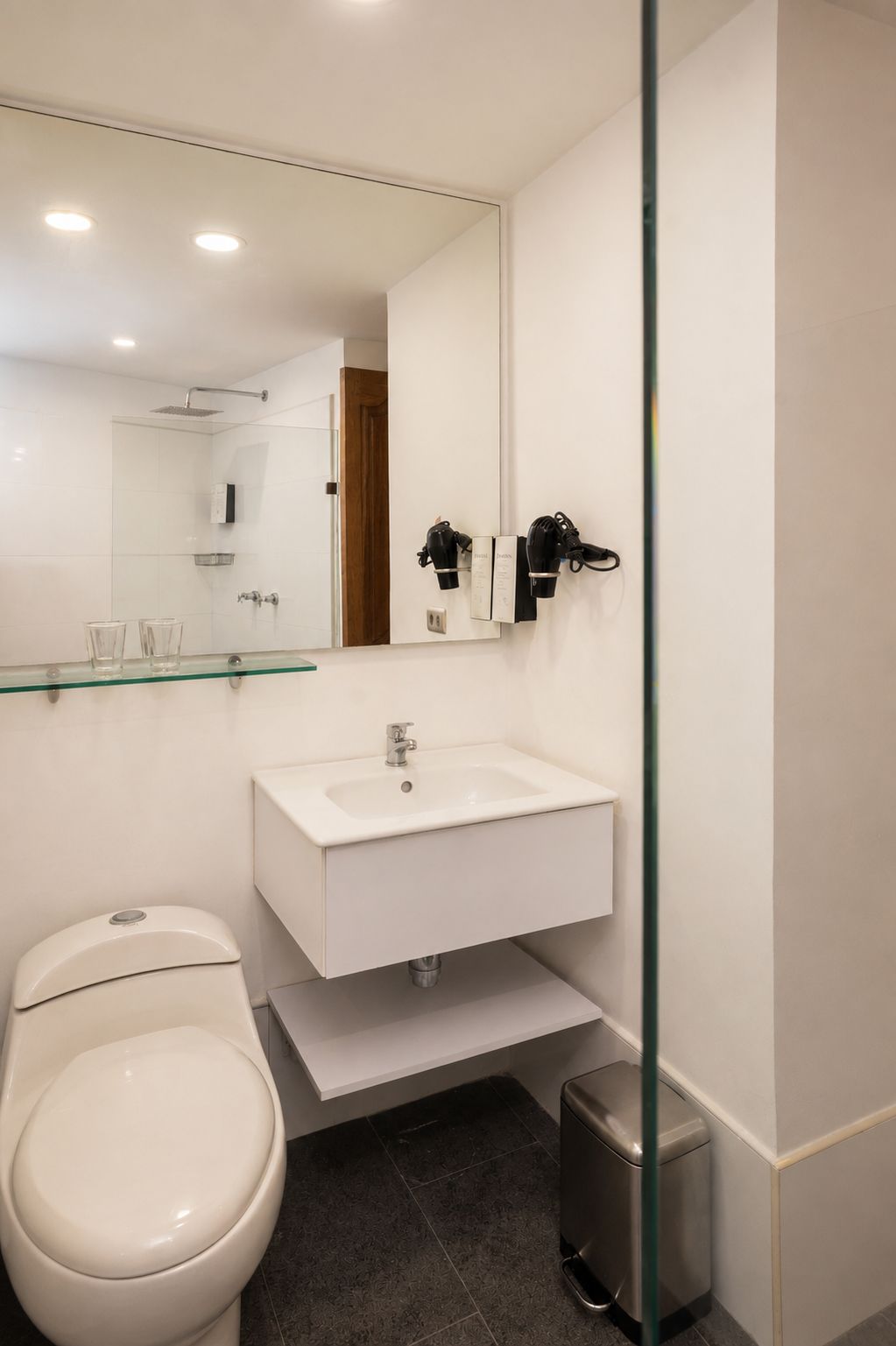 Un baño moderno con cabina de ducha de vidrio, un lavamanos blanco y un inodoro.