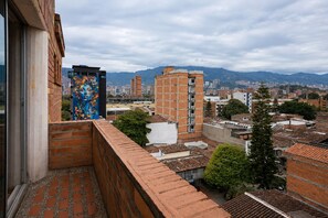 Un balcón con vista a un paisaje urbano, que incluye edificios y montañas al fondo.