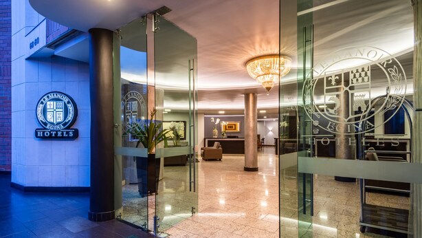 Un vestíbulo de hotel con puertas de vidrio, un mostrador de recepción y una araña.