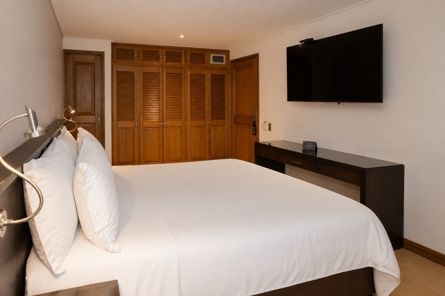 A bedroom with a bed, wooden wardrobe, a flat-screen TV, and a bedside table.