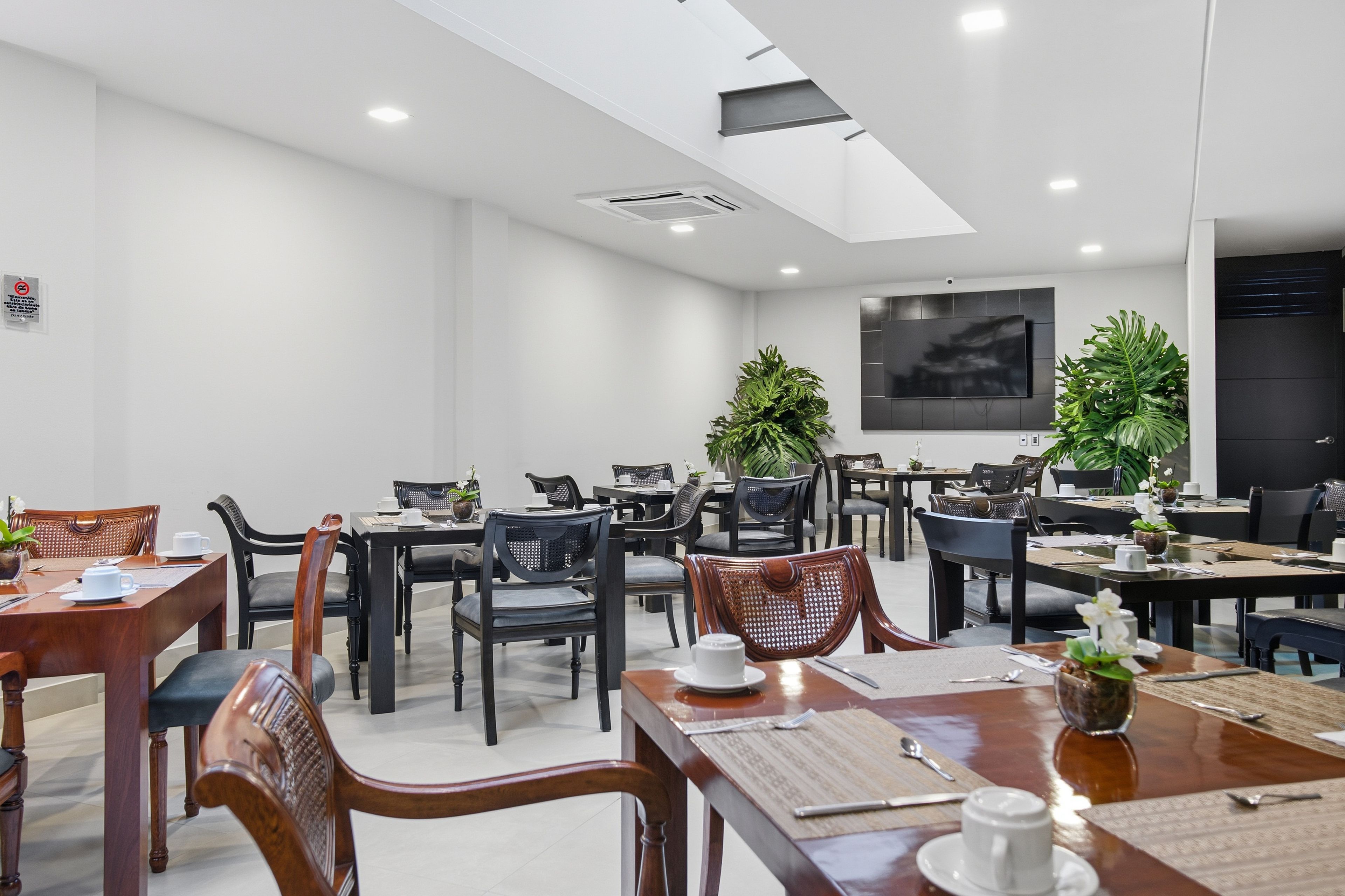 Una sala conferenze moderna con vari tavoli e sedie, dotata di tazze da caffè e un televisore a schermo piatto.
